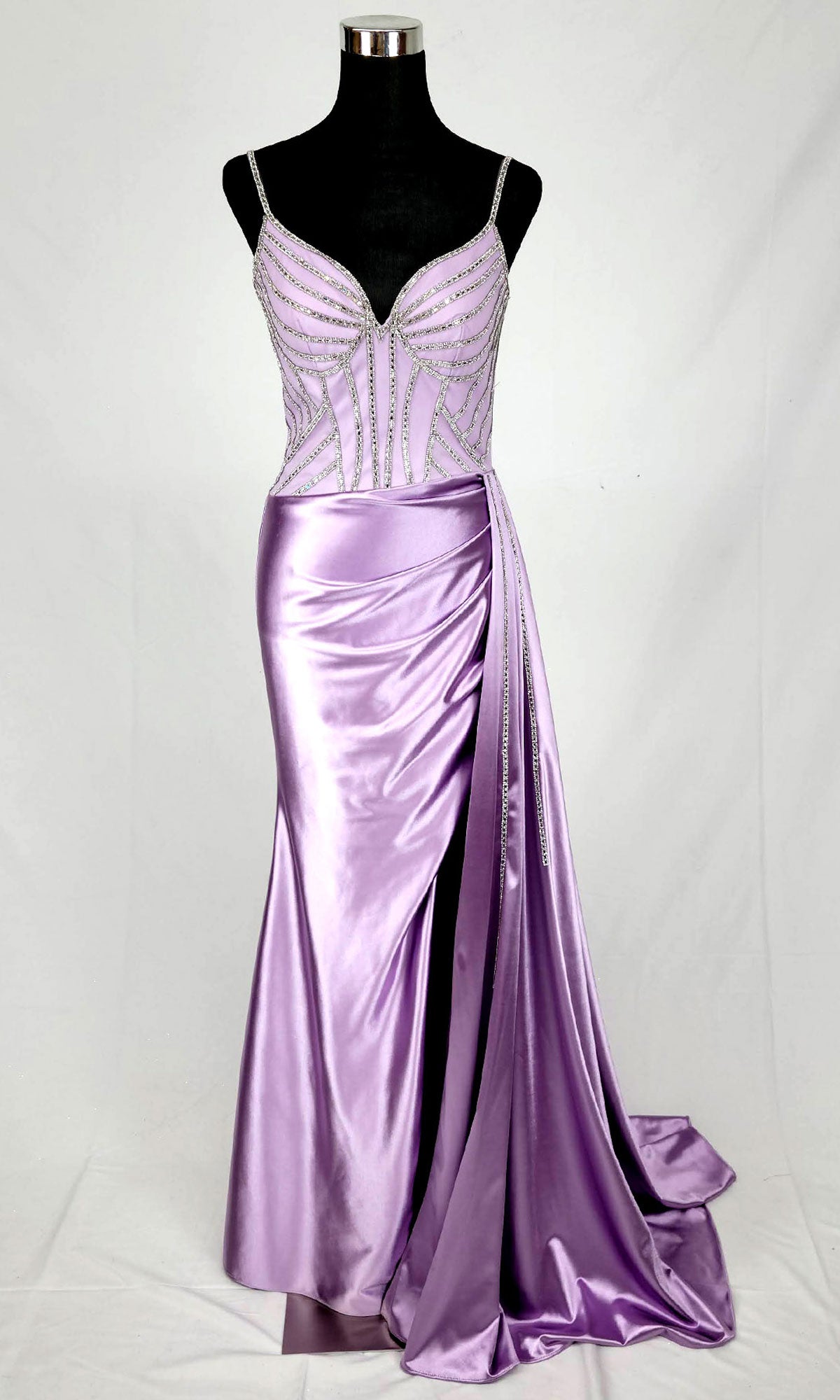 The Chicas C343 Side Sash Long Corset Prom Dress is a sleeveless lavender satin gown with beaded bodice, thin straps, high slit, and draped skirt, shown on a black mannequin.